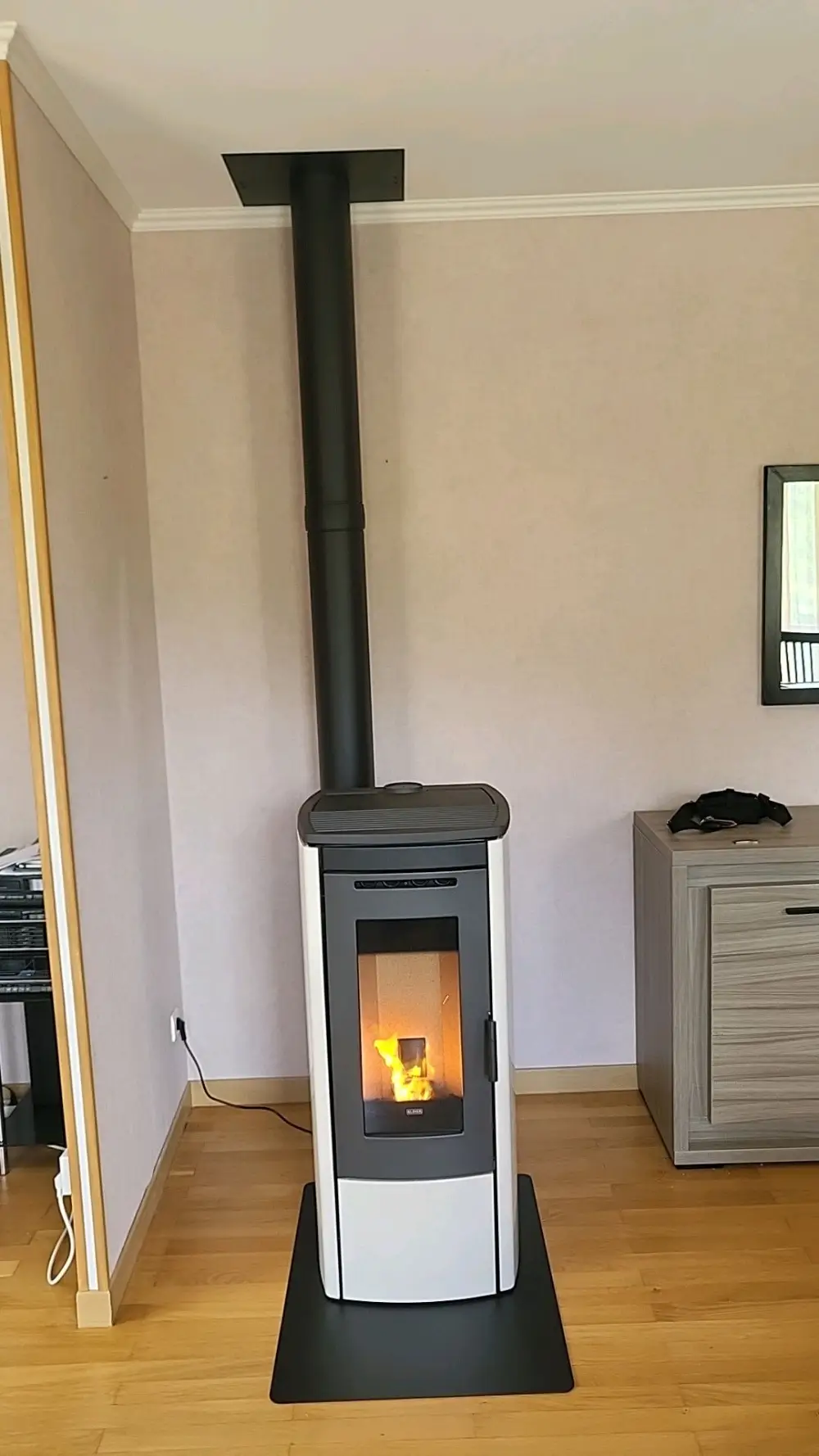 Poêle à granulés en fonctionnement de la marque Klover, modèle Soft 80, coloris blanc, sur une plaque de sol en acier noir
