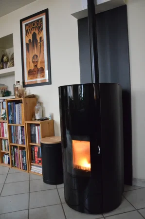 Poêle à granulés de la marque Jøtul de couleur noir en fonctionnement, avec une protection murale unie noir sur le mur d'adossement et un stockeur à granulés à côté.