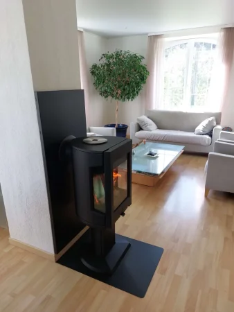 Poêle à bois bûches Jøtul F 167 avec vitres latérales, devant mur avec protection murale unie noire et plaque de sol en acier noir