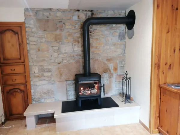 Poêle à bois bûches Jøtul F 305 sur pieds courts installé à la place d'une cheminée ancienne, le socle bas ayant été conservé