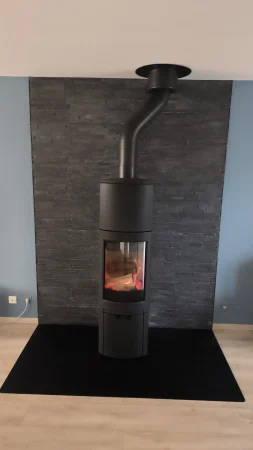 Poêle à bûches Jøtul F 378 avec réhausse et kit d'accumulation de chaleur, installé devant un mur recouvert d'un parement en pierre et sur une plaque de sol sur-mesure, recouvrant la base de l'ancienne cheminée